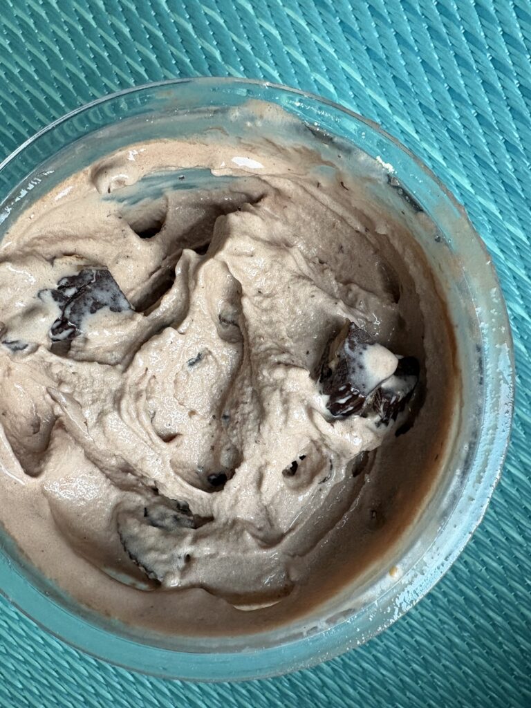 Chocolate mousse with visible cookie pieces in a glass bowl on a teal wicker surface.