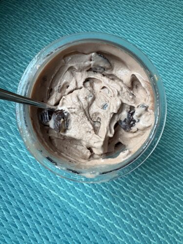 Chocolate mousse in a glass bowl with a spoon, set on a teal woven surface