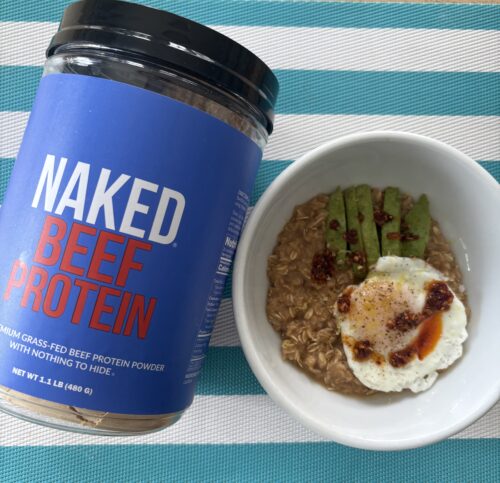 Blue tub of Naked Protein powder beside a bowl of oatmeal topped with apple slices on a turquoise striped mat.